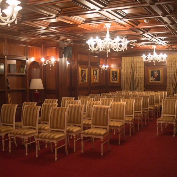 A room with rows of chairs, chandeliers, wooden paneling, and framed pictures on the walls.