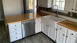 Una cocina con armarios blancos, encimera de madera, lavavajillas y fregadero.
