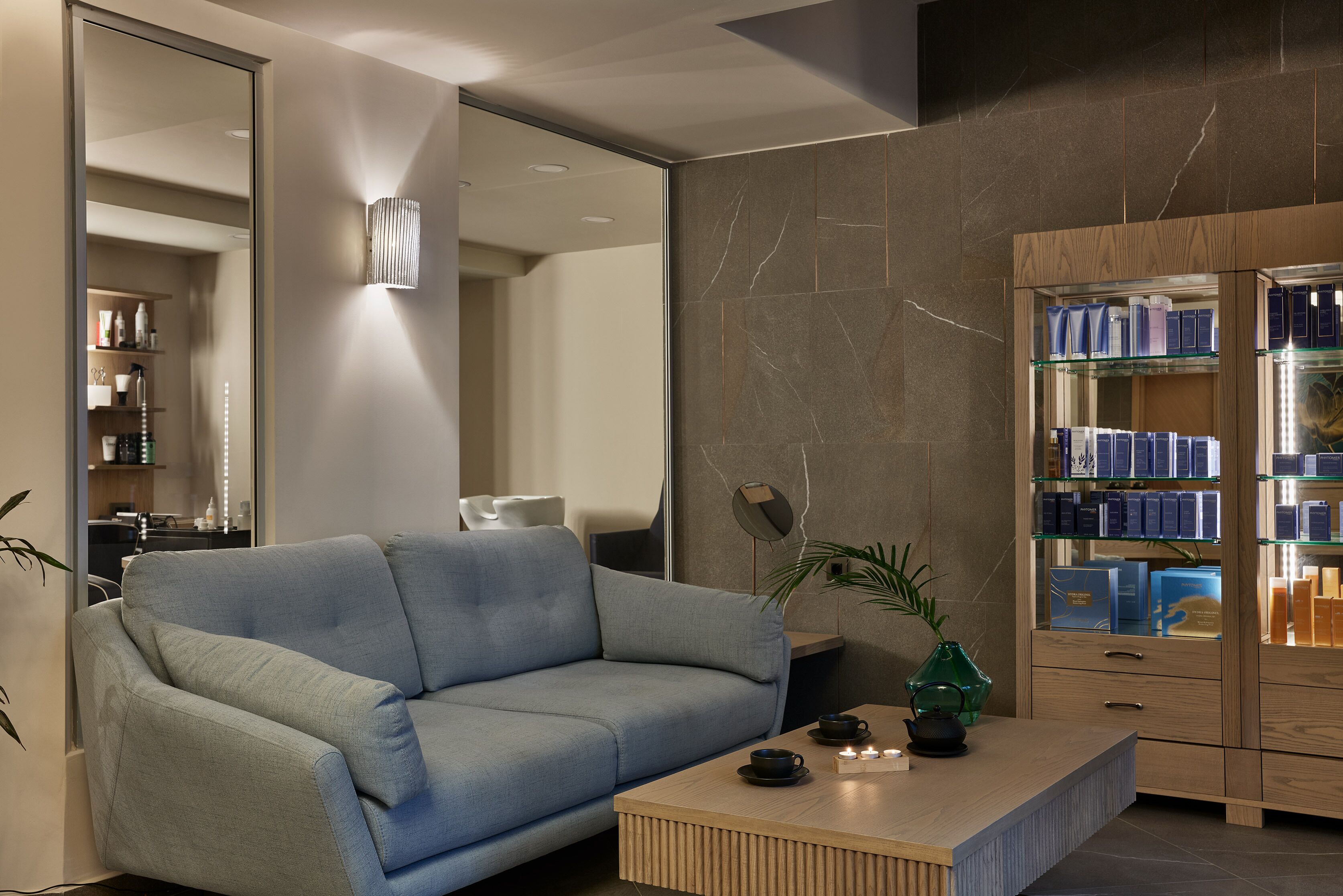 Una sala de estar moderna con un sofá azul claro, una mesa de centro de madera y un armario de vidrio con artículos de aseo.