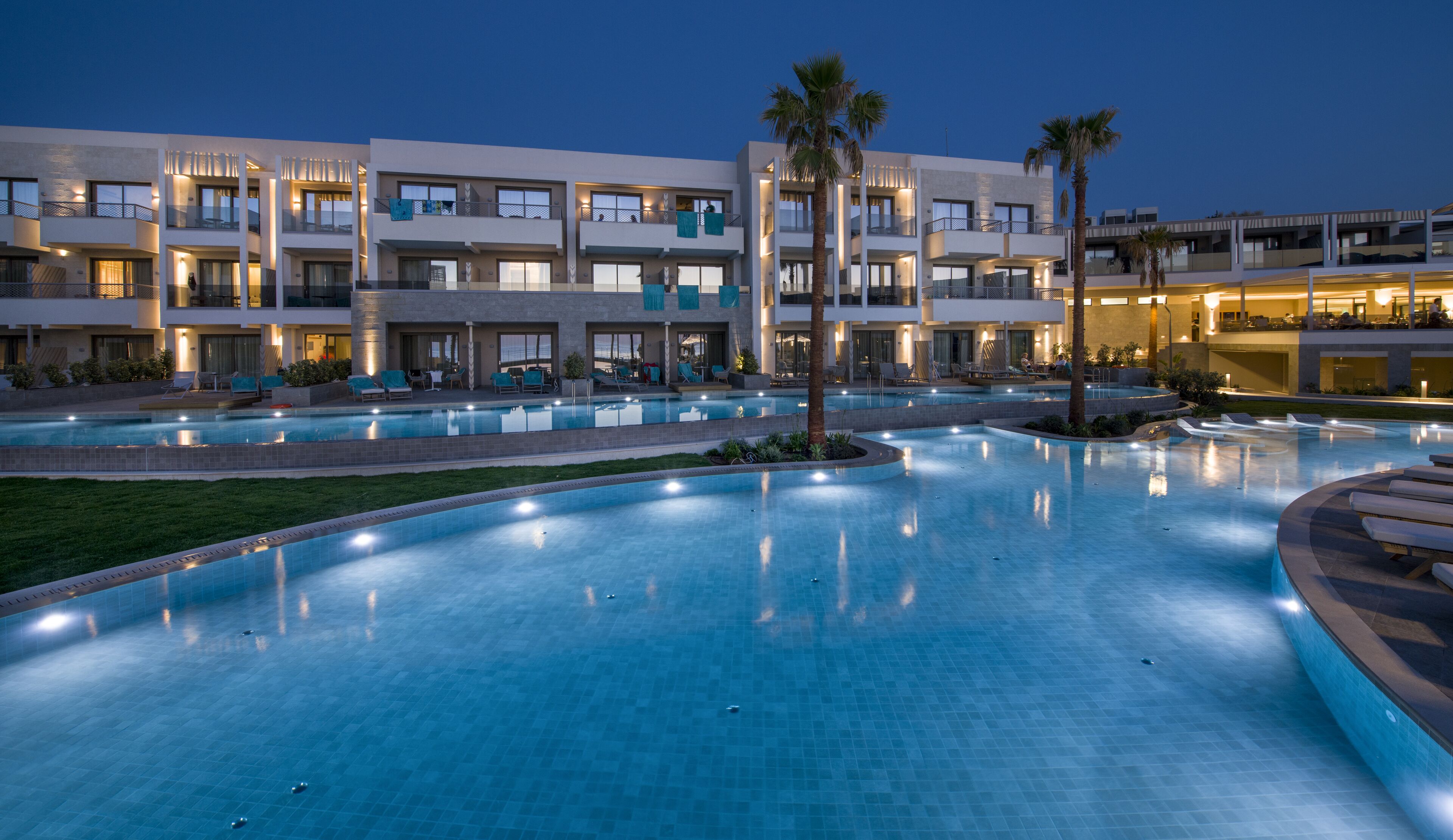 Un hotel moderno con varios balcones, una piscina grande y zonas exteriores bien iluminadas.
