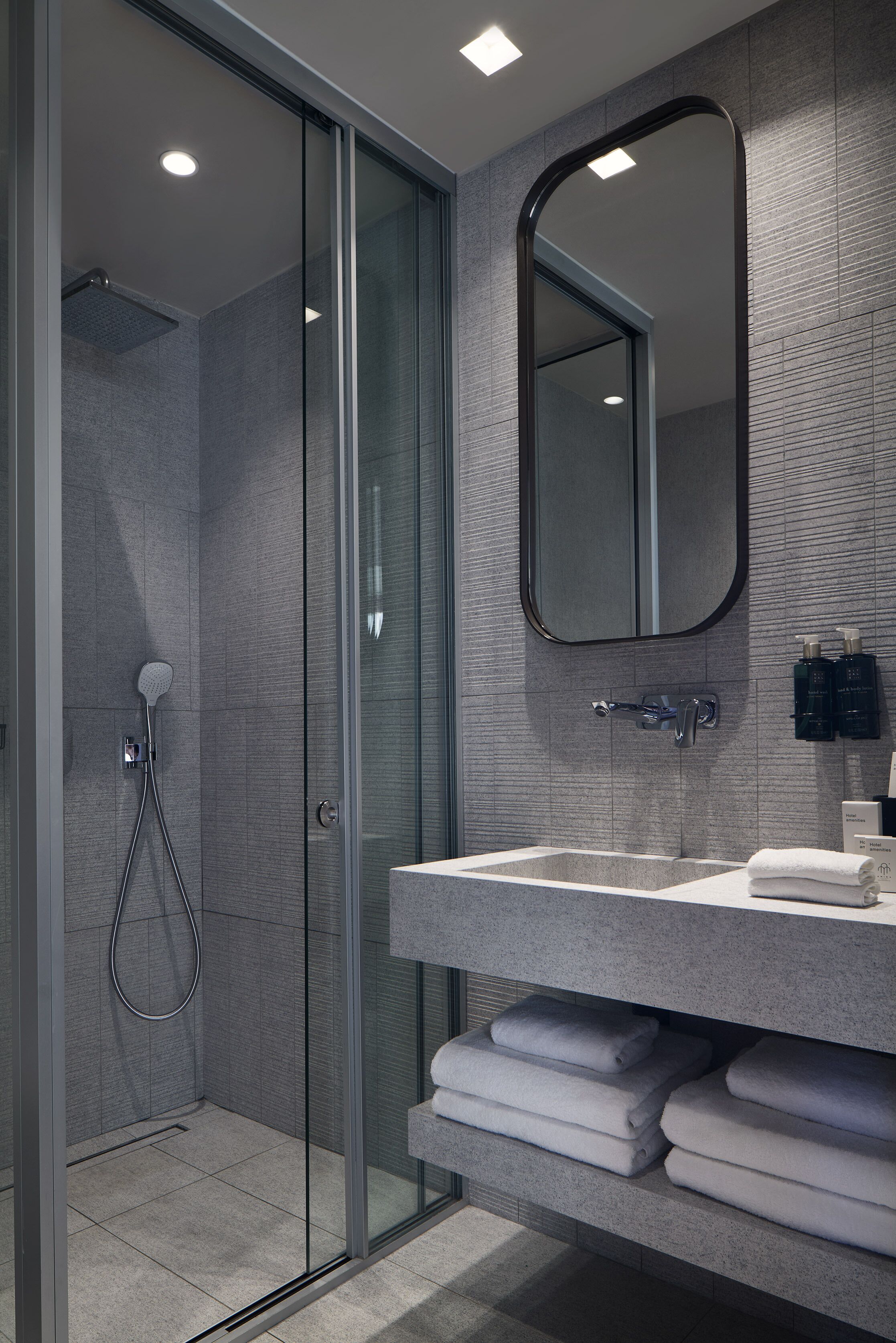 Un bagno moderno con box doccia in vetro, uno specchio grande e lavabo incassato con portasciugamani.