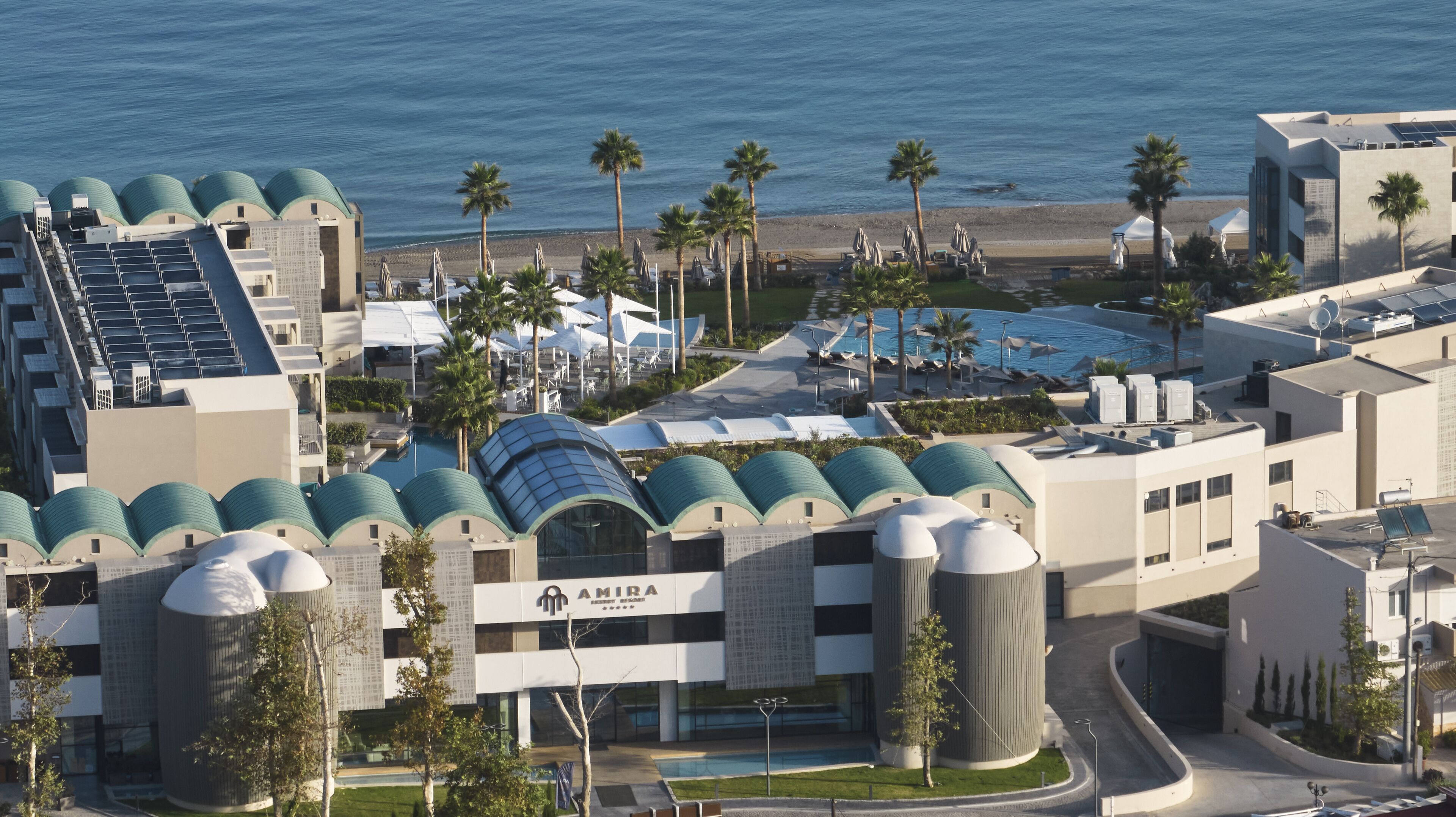 A modern hotel with a pool, palm trees, and a beach view.