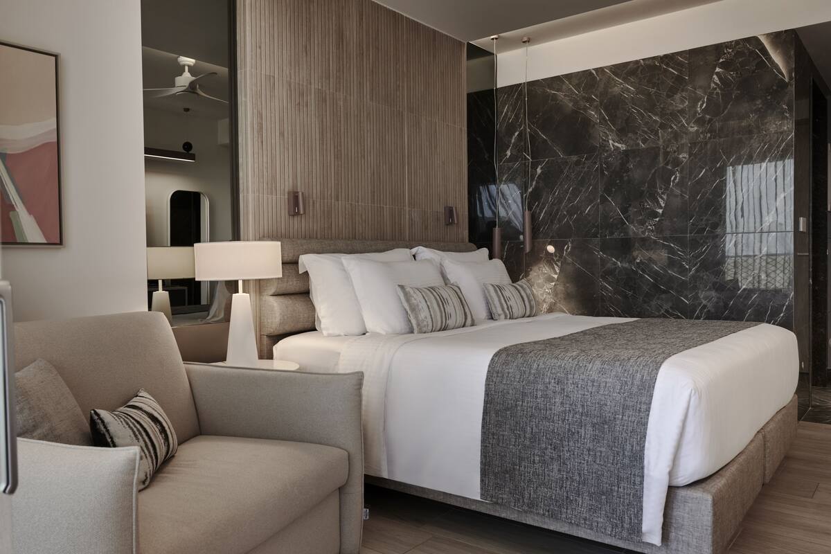 A modern bedroom with a large bed, a bedside table with a lamp, a sofa, and a large mirror.