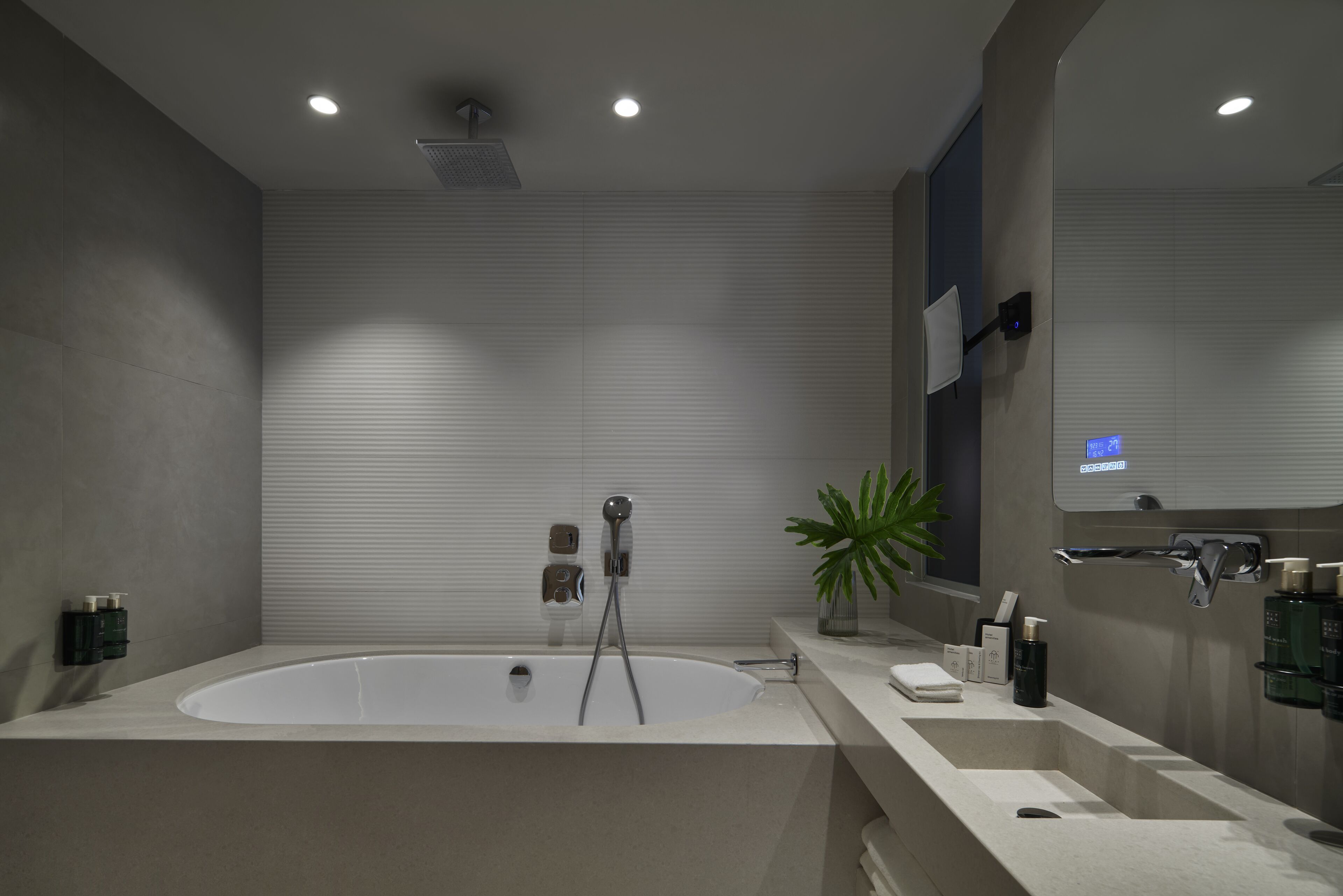 Un baño moderno con una bañera independiente, un cabezal de ducha y una planta grande en maceta.