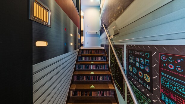 Eine moderne Treppe mit Bücherregalen an beiden Seiten, einem Metallgeländer und einer Wand mit einem digitalen Bildschirm.