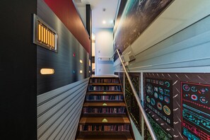 A modern staircase with bookshelves on either side, a metal railing, and a wall with a digital display. - GUEST HOUSE DISCOVERY SHIP (Kyoto)