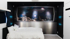 Ein Schlafzimmer mit einem großen, an der Wand befestigten Fernseher, der eine Weltraum-Szene zeigt, einem Bett mit weißer Bettwäsche und einem modernen Design mit dunklen Wänden und metallischen Akzenten.