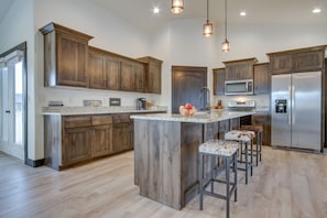 A modern kitchen with wooden cabinets, a large island, bar stools, stainless steel appliances, and pendant lighting. - 1 Mi to Beaverhead River: Mtn-View Dillon Retreat (Dillon)