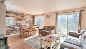Un ampio soggiorno con parete in legno, una zona pranzo con tavolo e sedie, un divano e un'ampia porta-finestra che dà su un balcone.