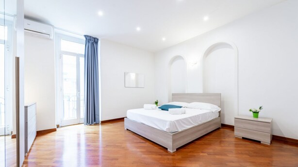 Ein modernes Schlafzimmer mit einem großen Bett, einem Nachttisch, einem Spiegel und einem Fenster mit Vorhängen.