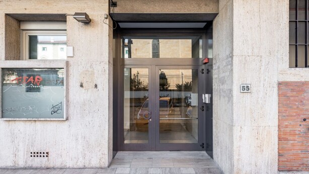 A building entrance with a glass door, a number '55' sign, and a window with graffiti. - GuestHost - Functional 22sqm studio apartment that can accommodate 2 people. Located on the first floor, with elevator (not suitable for disabled people), of a building in San Lorenzo neighborhood, the studio is about 15 minutes walk away from Santa Mari (Firenze)