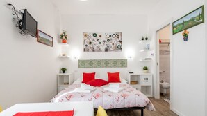 A modern bedroom with a bed, bedside tables, a TV mounted on the wall, and a bathroom visible through an open door. - GuestHost - Functional 22sqm studio apartment that can accommodate 2 people. Located on the first floor, with elevator (not suitable for disabled people), of a building in San Lorenzo neighborhood, the studio is about 15 minutes walk away from Santa Mari (Firenze)