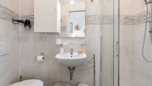 A modern bathroom with a glass shower enclosure, a white sink with a mirror above, and a toilet. - GuestHost - Functional 22sqm studio apartment that can accommodate 2 people. Located on the first floor, with elevator (not suitable for disabled people), of a building in San Lorenzo neighborhood, the studio is about 15 minutes walk away from Santa Mari (Firenze)
