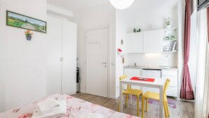 A bedroom with a bed, a desk, and a chair in a room with white walls and a door. - GuestHost - Functional 22sqm studio apartment that can accommodate 2 people. Located on the first floor, with elevator (not suitable for disabled people), of a building in San Lorenzo neighborhood, the studio is about 15 minutes walk away from Santa Mari (Firenze)