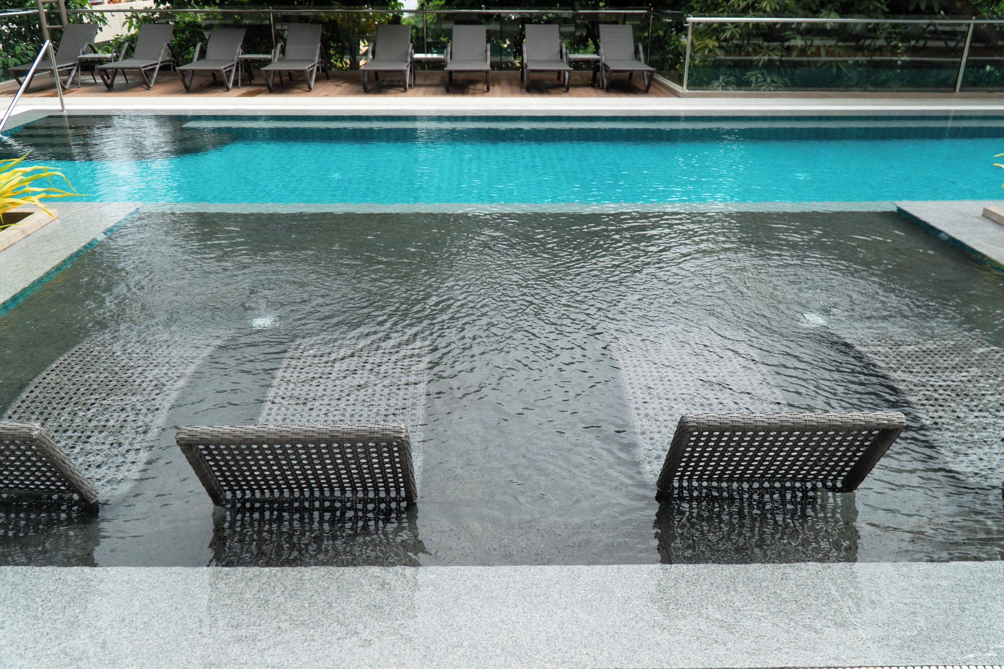 A swimming pool with clear water, surrounded by lounge chairs and a tiled deck.