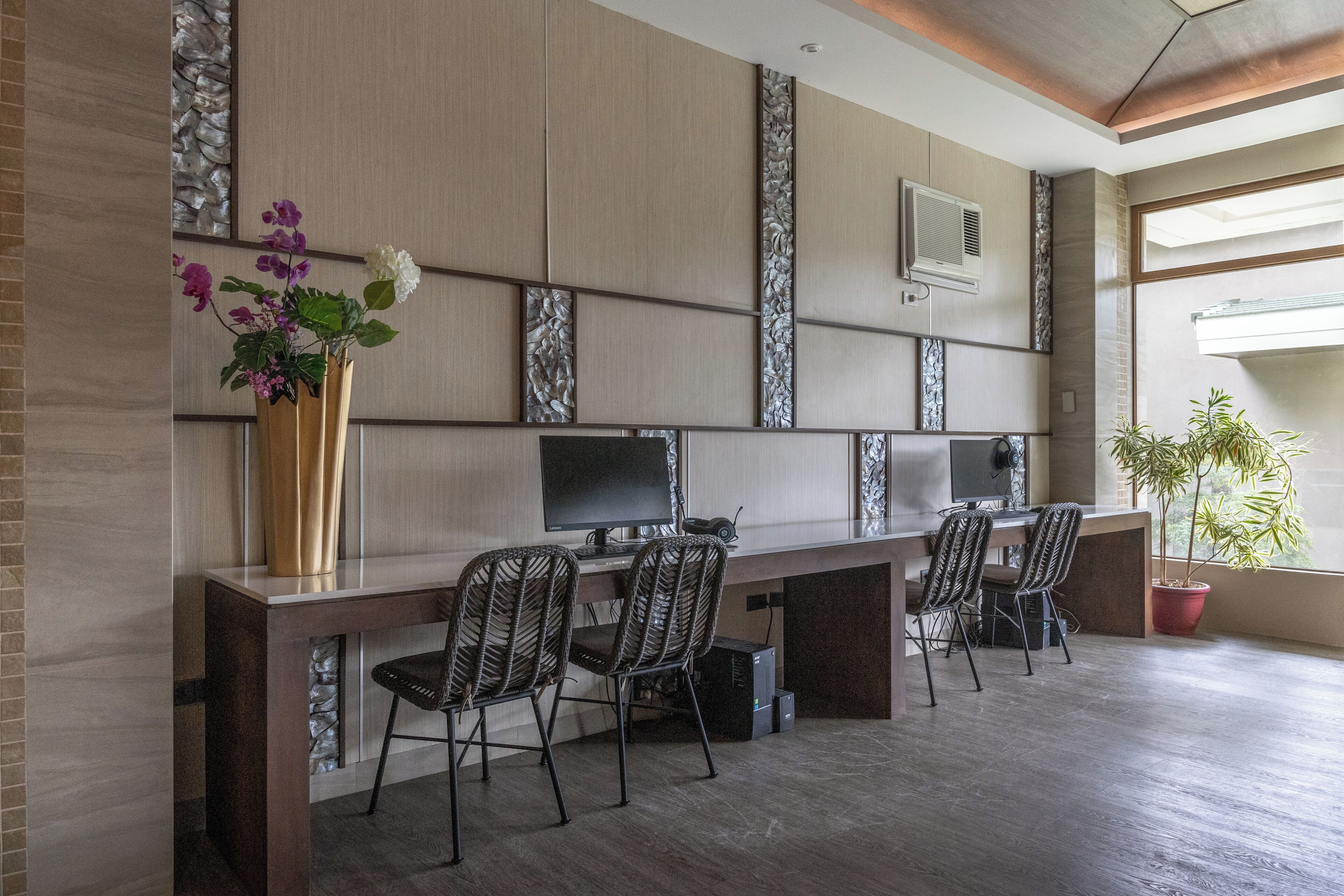 A modern office space with a long table, four chairs, a large vase with flowers, and a potted plant.