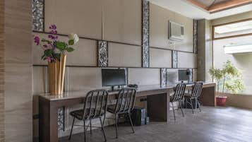 A modern office space with a long table, four chairs, a large vase with flowers, and a potted plant.
