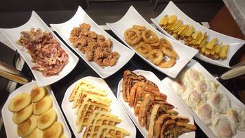 Una mesa de buffet con diversos platos, incluyendo pollo frito, aros de cebolla, alitas de papa, gofres y huevos.