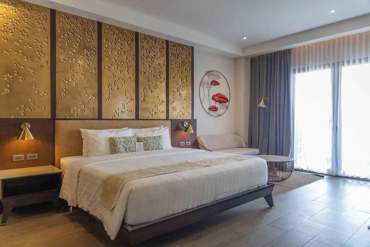 A modern hotel room with a large bed, a bedside table, a chair, and a decorative wall panel.