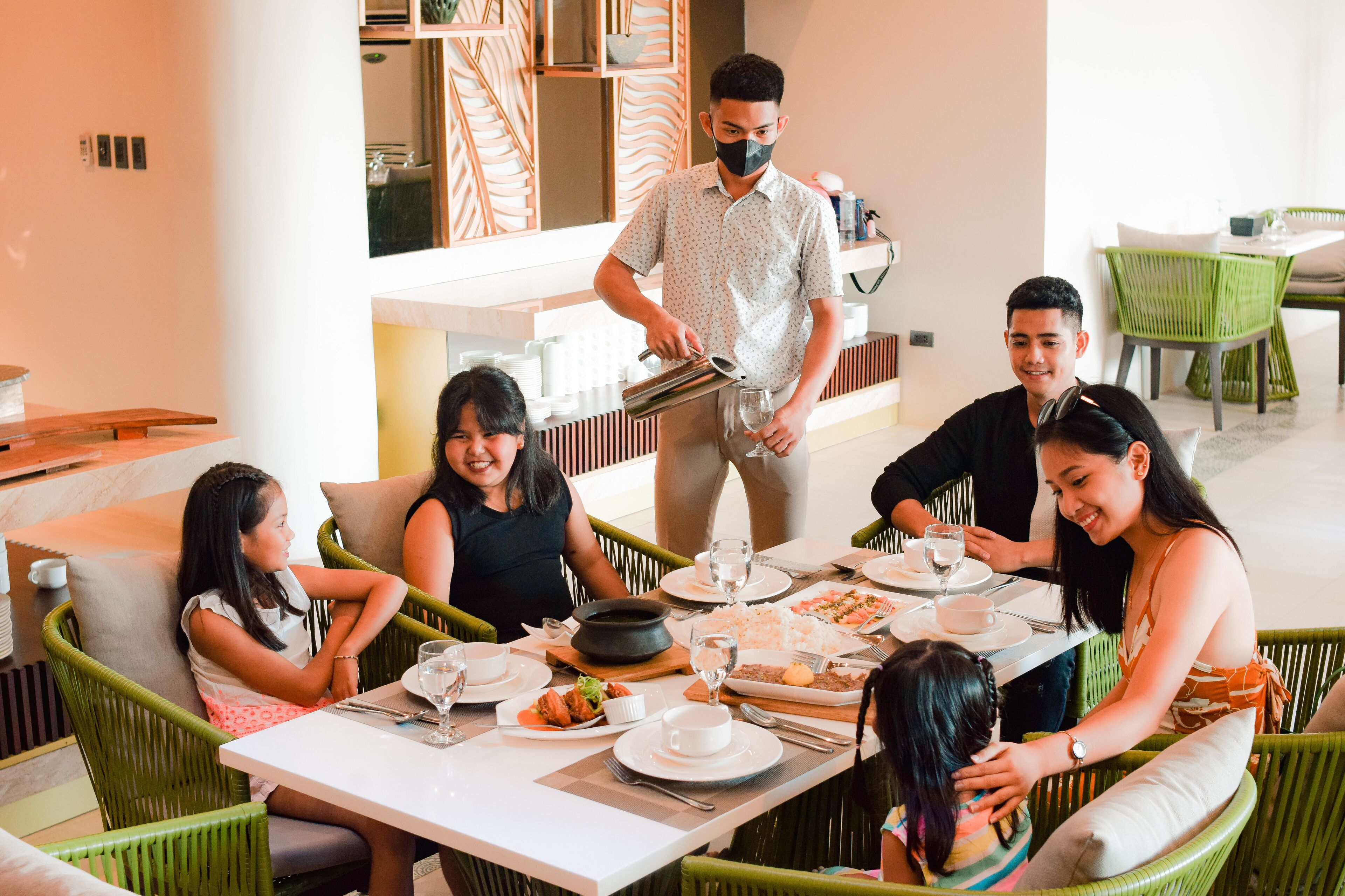 A group of people dining at a restaurant with a waiter serving food.
