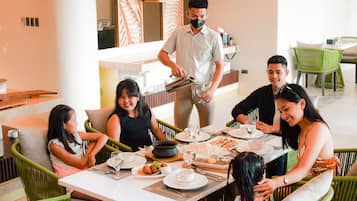 A group of people dining at a restaurant with a waiter serving food.