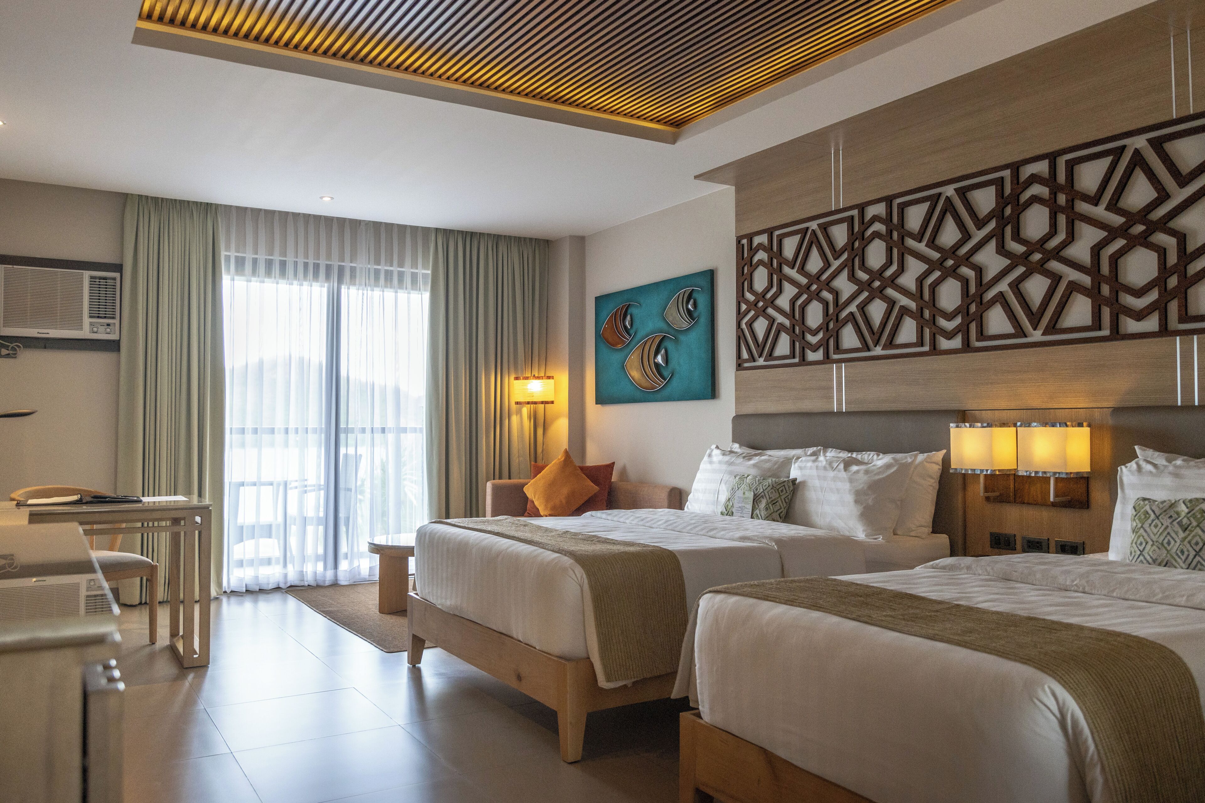 A hotel room with two beds, a desk, and a view of the outdoors.