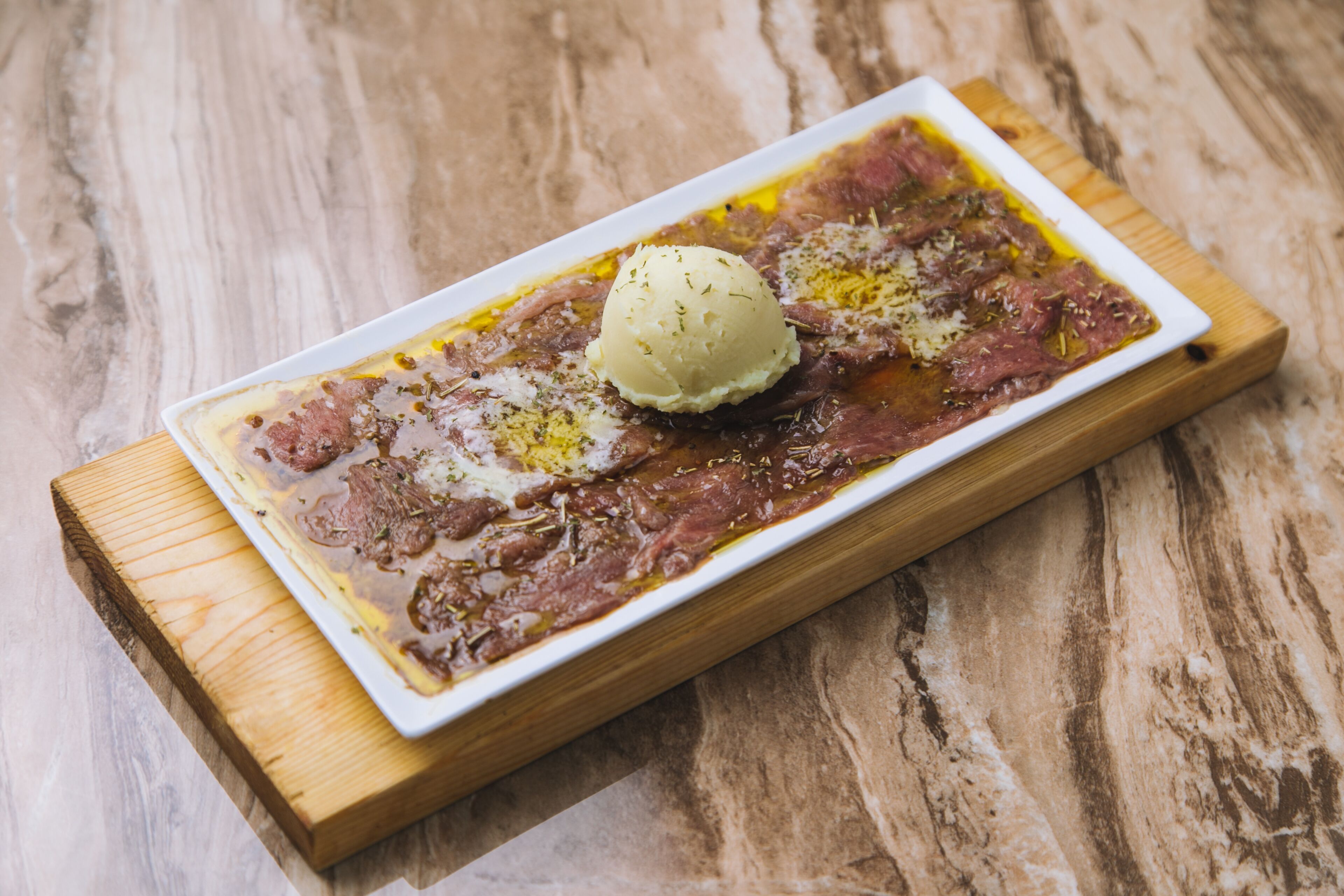 A rectangular white plate with a serving of meat and a scoop of ice cream on a wooden board.