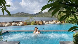 Zona de piscina con una persona en el agua, rodeada de exuberante vegetaci ón y vistas a un lago y colinas.