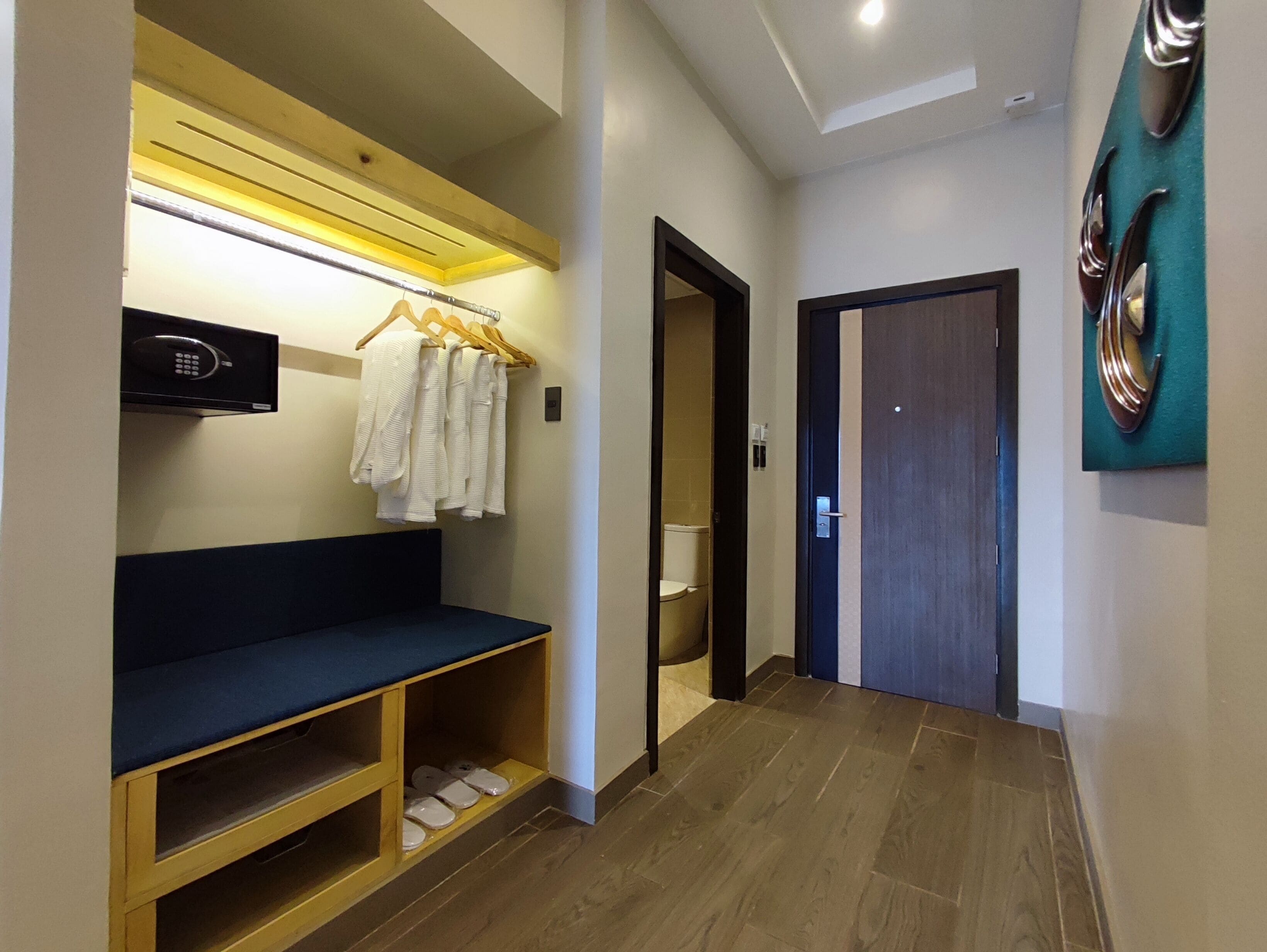 Un couloir avec un banc, un porte-manteau sur lequel sont suspendus des vêtements, des toilettes et une porte.