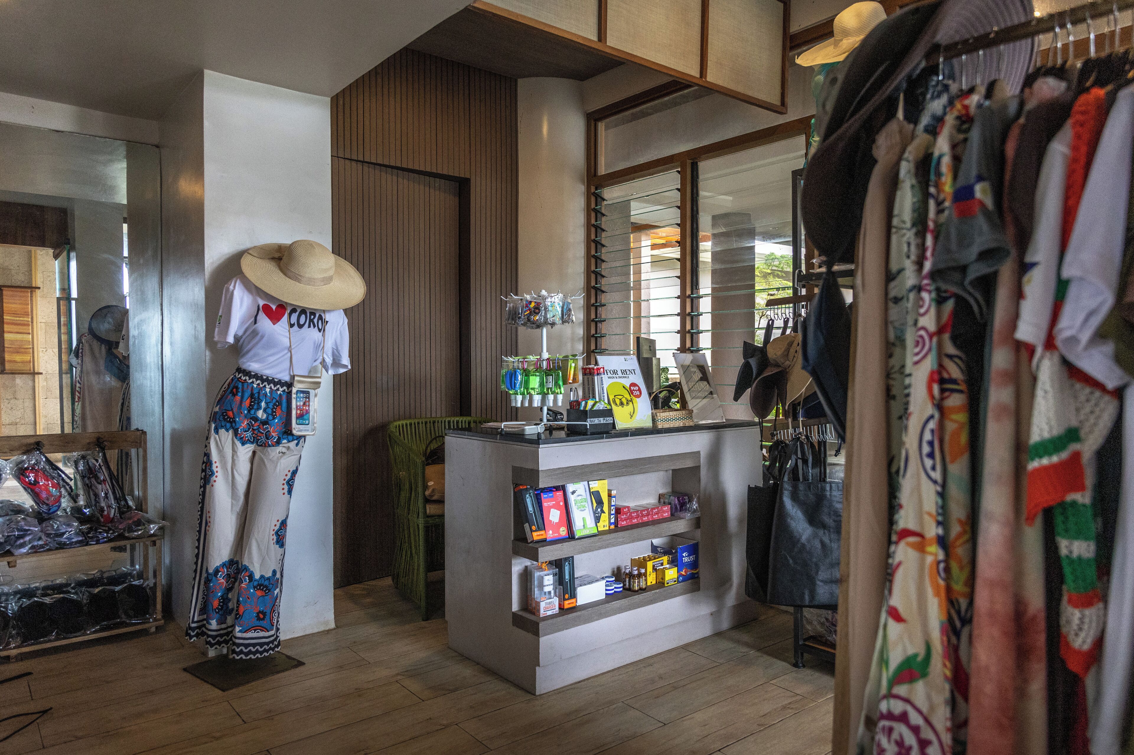 A clothing store with a mannequin wearing a hat and patterned pants, shelves with various items, and a display of hats.