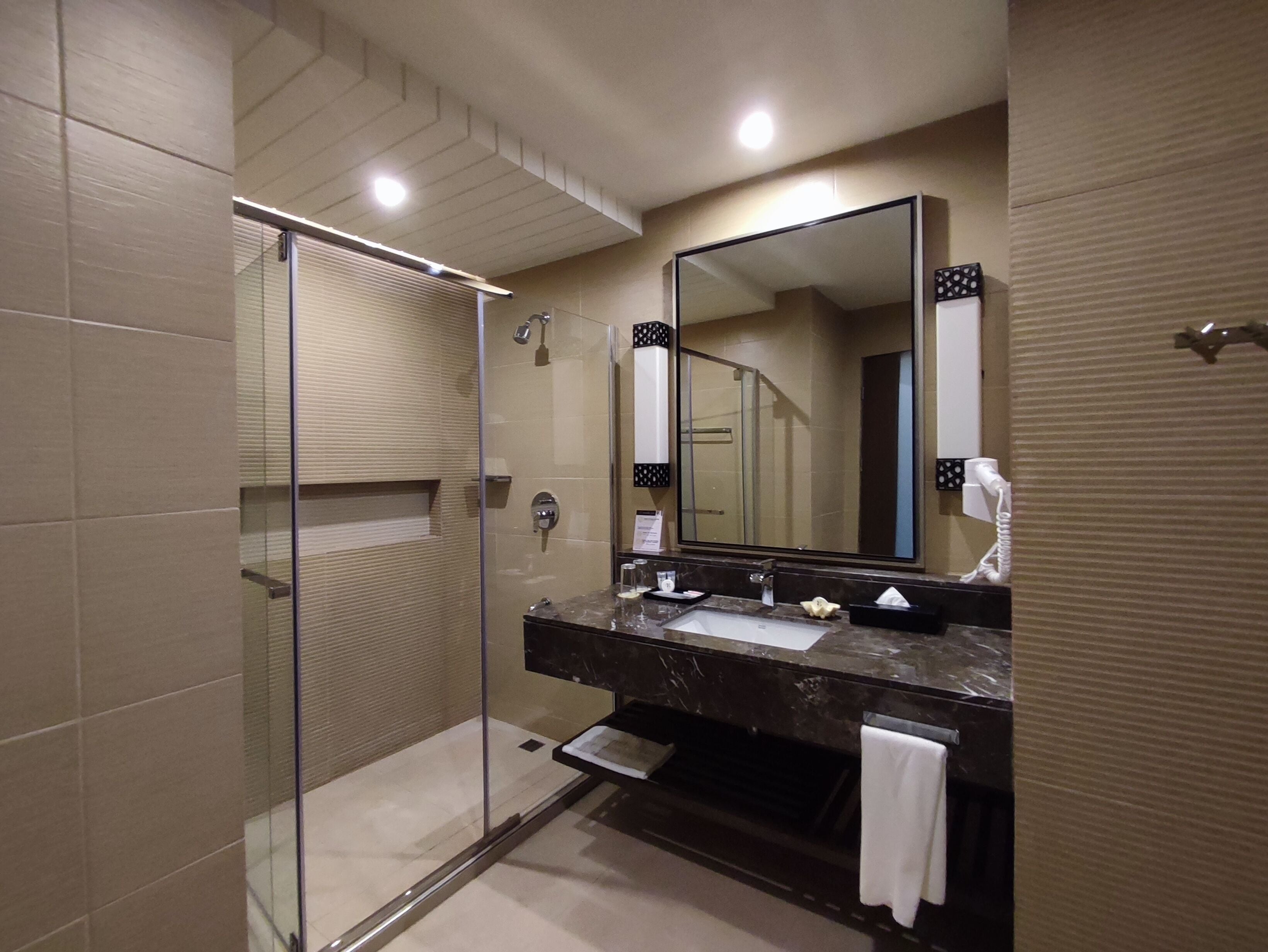 Un baño moderno con ducha de vidrio, un espejo grande y encimera de mármol.