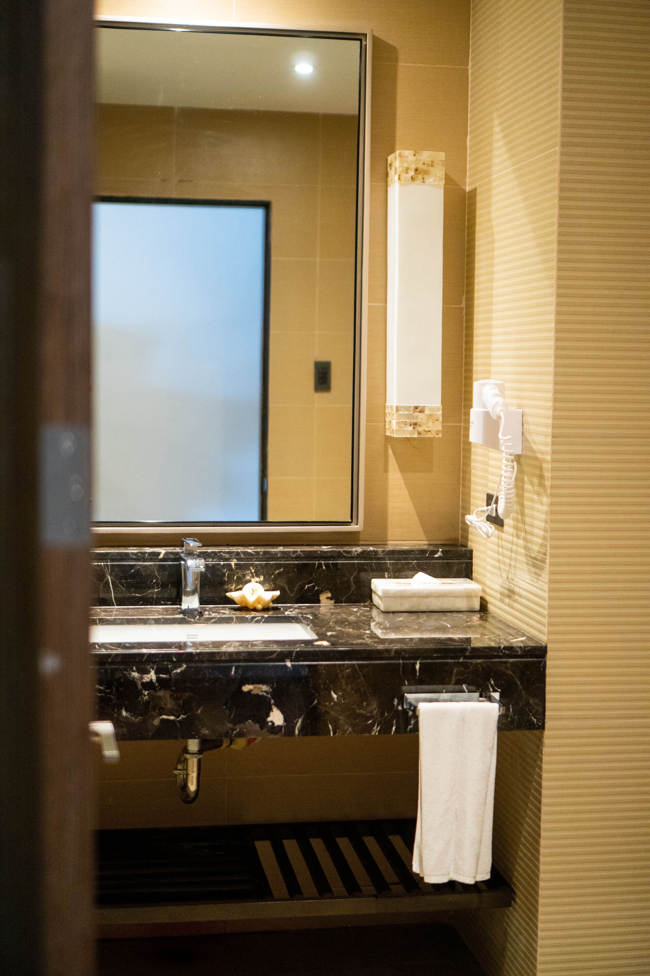 A bathroom with a marble sink, a mirror, a towel rack, and a hand dryer.