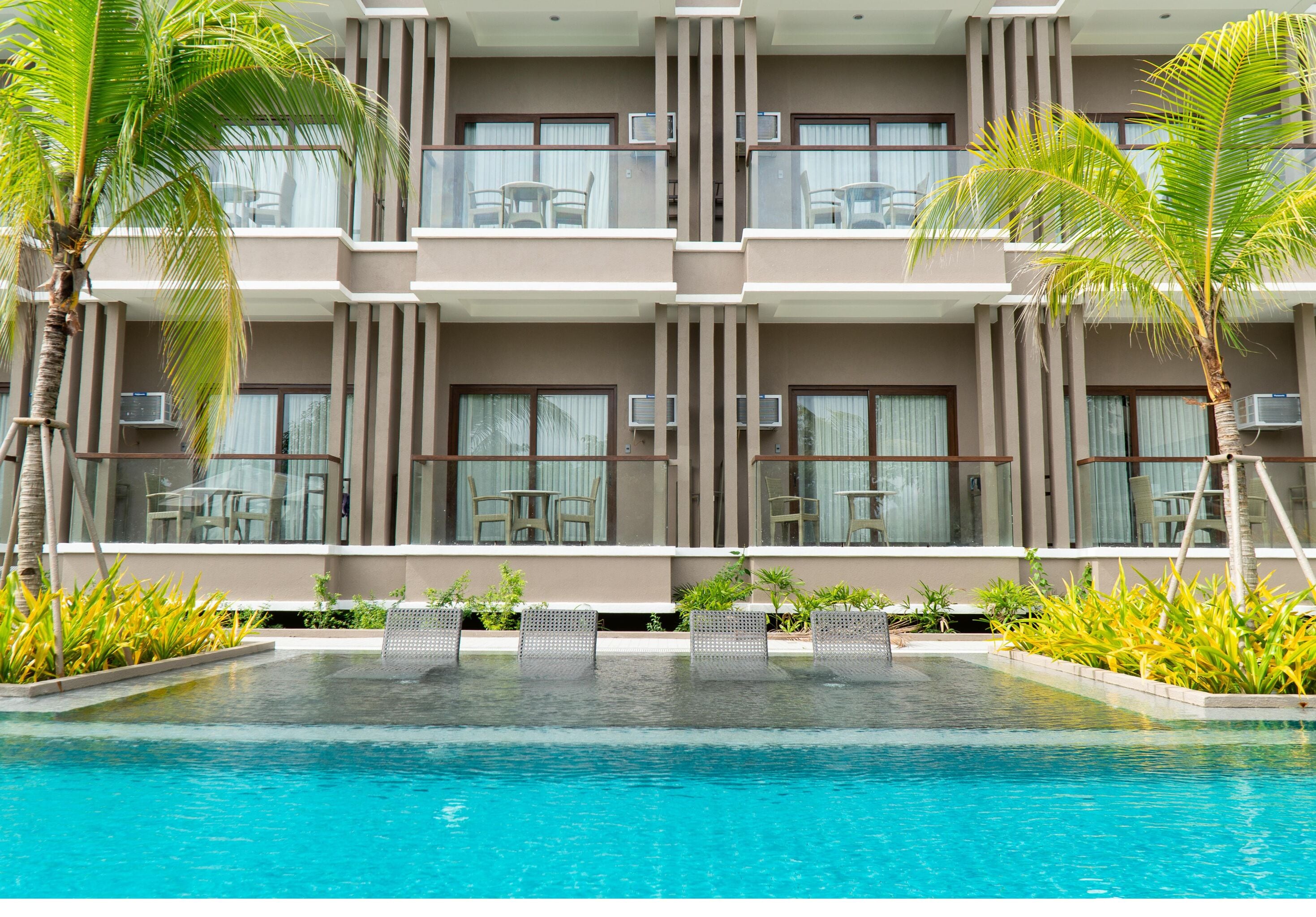 A hotel with a swimming pool, outdoor seating, and palm trees.