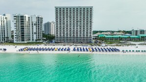 Un hotel frente a la playa con varios edificios altos al fondo, una playa de arena y numerosos paraguas.