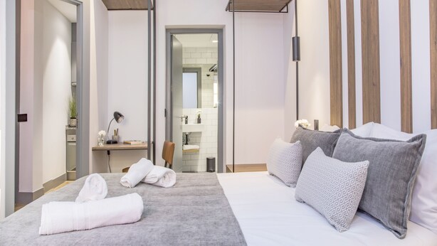 A modern hotel room with a large bed, a desk, and a bathroom visible through an open door. - Incredible 1 bedroom apartment at El Rastro (Madrid)