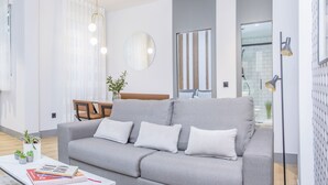 A modern living room with a grey sofa, a coffee table with books, a round mirror, and a floor lamp. - Incredible 1 bedroom apartment at El Rastro (Madrid)