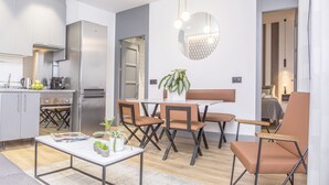 A modern kitchen with stainless steel appliances, a dining area with a white table and brown chairs, and a small seating area with a bench and a single chair. - Incredible 1 bedroom apartment at El Rastro (Madrid)