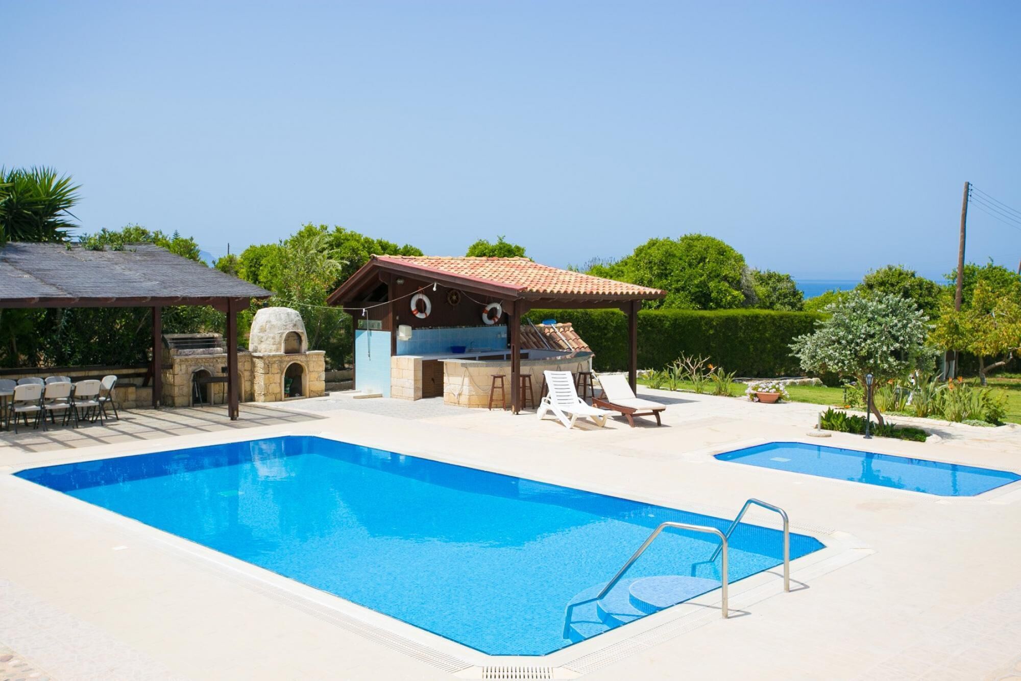 Area piscina con due vasche, posti a sedere all'aperto, un barbecue e vista mare.