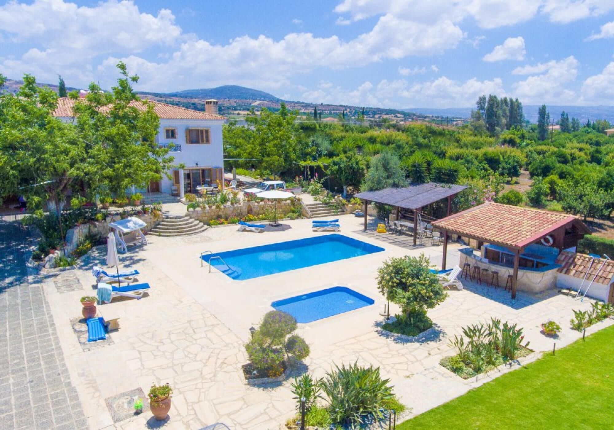 Una villa con una amplia piscina exterior, un porche cubierto y vistas del paisaje circundante.