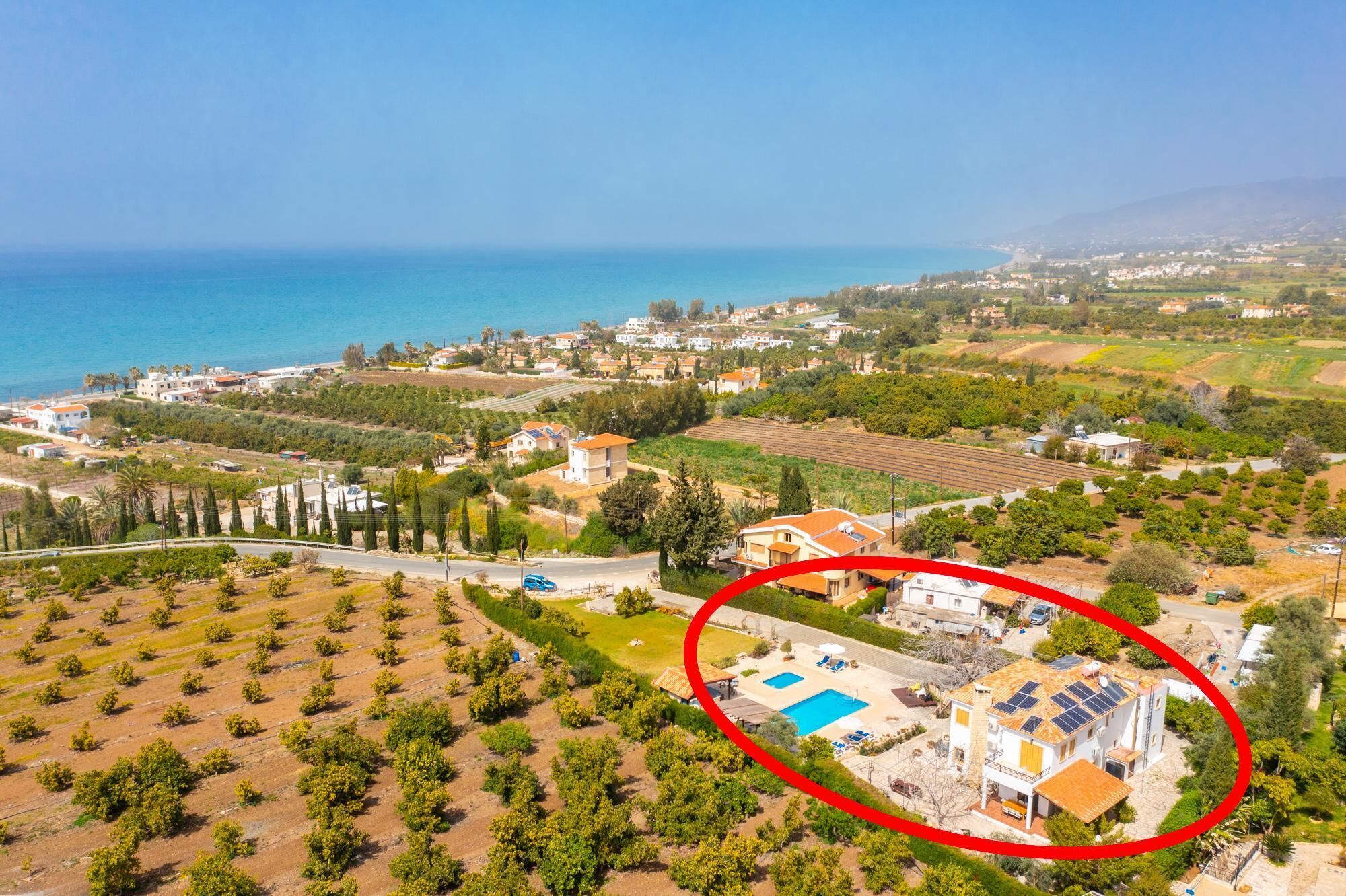 An aerial view of a coastal area with a house circled, featuring a swimming pool and solar panels.