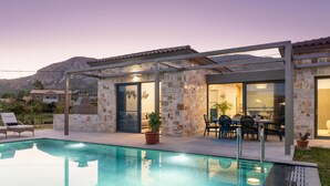 A modern outdoor pool area with a pergola, stone walls, and a dining area with chairs and tables. - Villa Ersi in Ionian Islands (Kefalonia)
