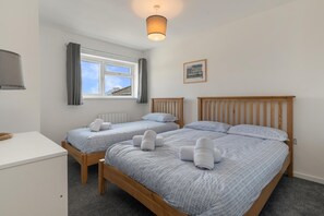 A hotel room with two wooden beds, a desk, a window with curtains, and a wall-mounted lamp.