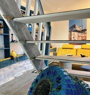 Une pièce avec un escalier, un canapé jaune et une chaise bleue.