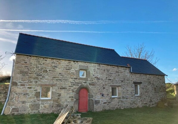 Un bâtiment en pierre avec une porte rouge, une petite fenêtre et un toit en pente.