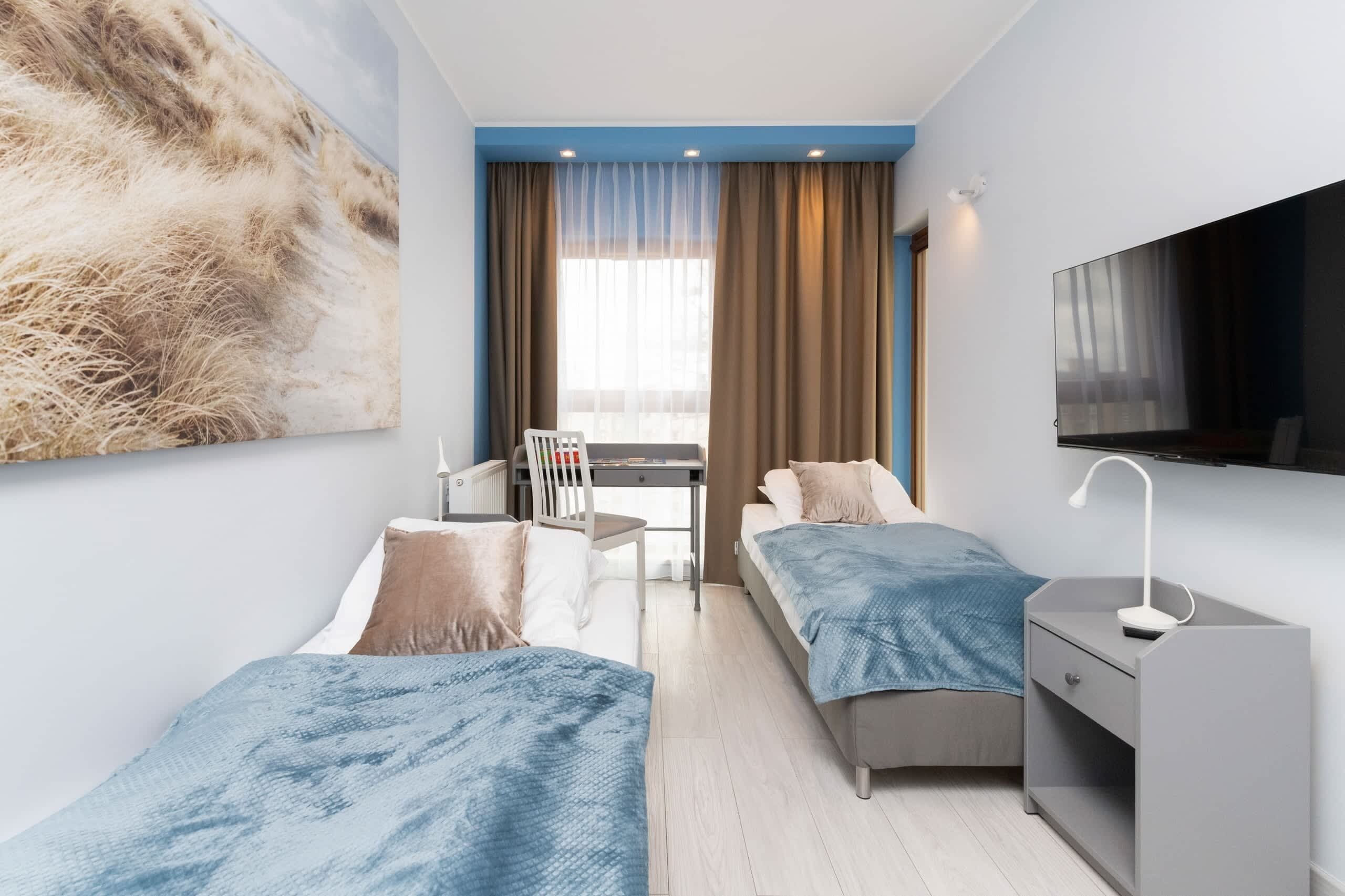 Een moderne hotelkamer met twee bedden, een bureau, een stoel, een televisie en een groot raam met gordijnen.