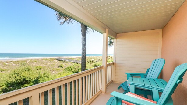 Een balkon met uitzicht op het strand, twee turquoise Adirondack-stoelen en een houten leuning.