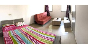 A bedroom with a bed, a sofa, a small table, and a window.