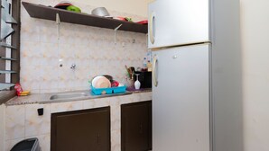 A compact kitchen with a refrigerator, sink, and a shelf above the countertop.