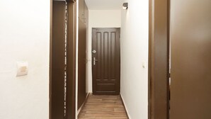A narrow hallway with wooden flooring and a dark brown door at the end.