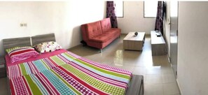 Un dormitorio con cama, sofá, mesita y ventana.